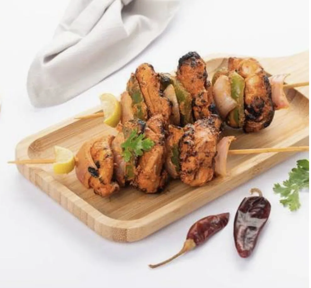 Chicken tikka skewers with onion, capsicum and lemon on a wooden board
