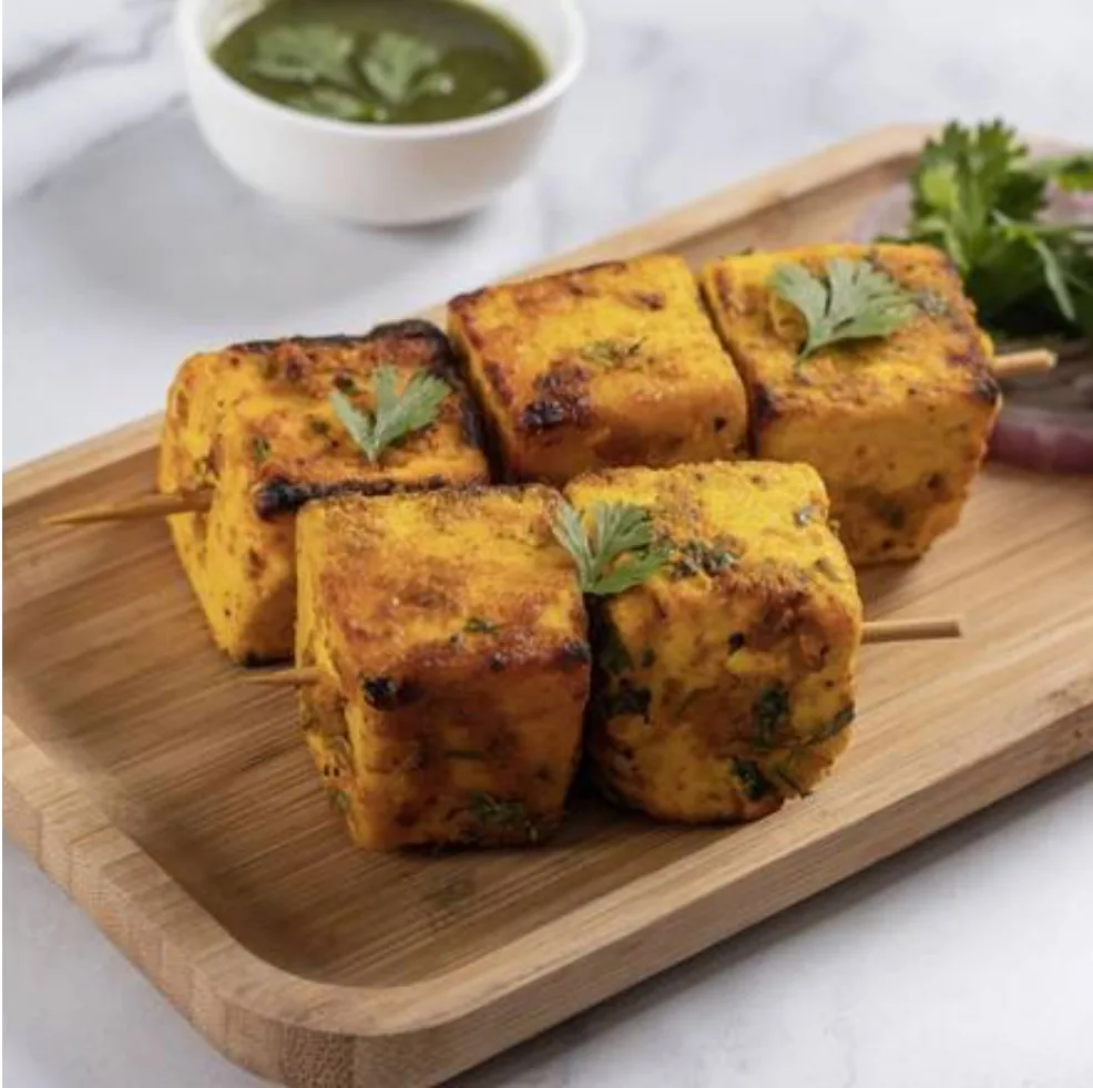 Paneer tikka skewers on a wooden tray with green chutney