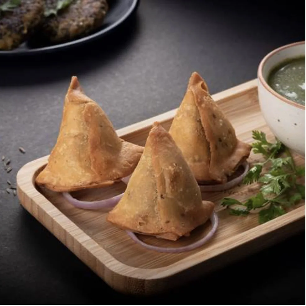 Three samosas on a wooden tray with green chutney