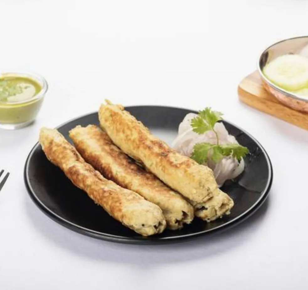 Seekh kebabs on a black plate with chutney and onion